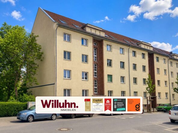 Five-story beige apartment building with red brick columns and a large Willuhn Immobilien banner across the street.