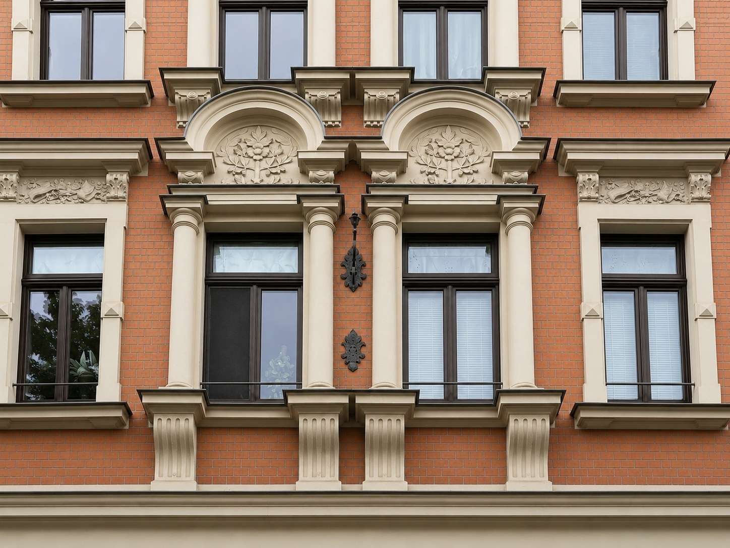 Ornate red brick building facade with beige stone arches, columns, and decorative reliefs around the windows.