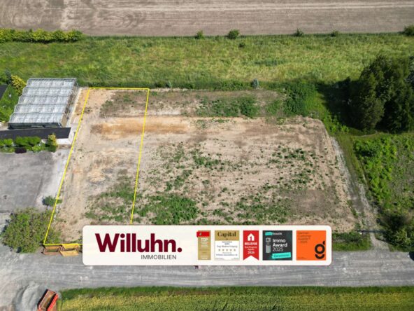 Aerial view of a vacant lot outlined in yellow beside a greenhouse, with a large Willuhn Immobilien sign at the edge of the frame.