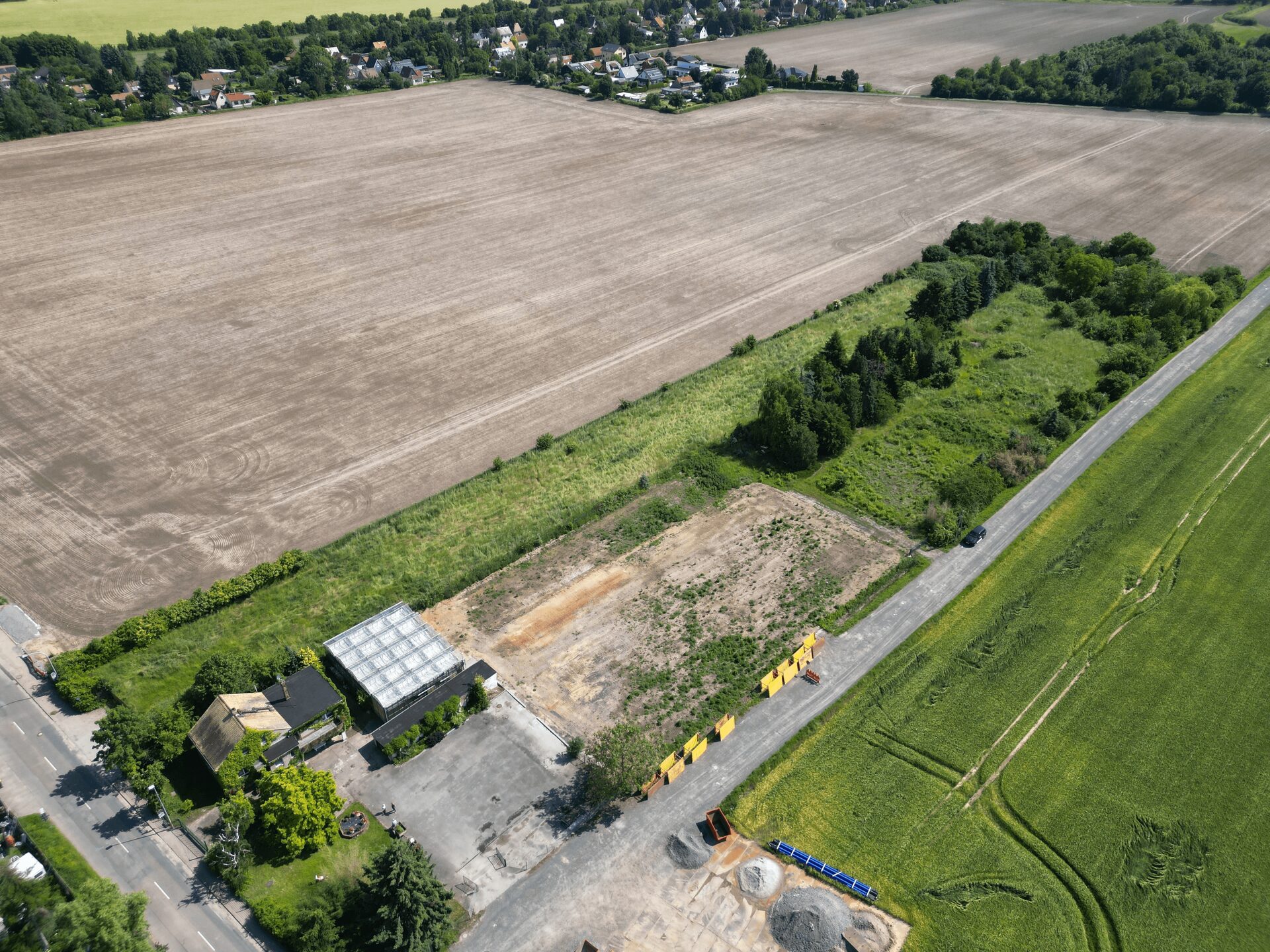 Aerial view of a large harvested field bordered by a road, with a small village and trees in the distance.