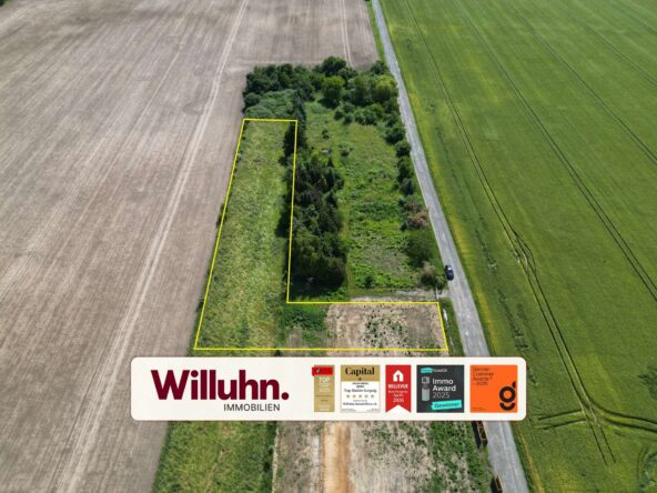 Aerial view of a rectangular land parcel outlined in yellow between fields and a road, with trees along the edge and a Willuhn Immobilien sign at the bottom