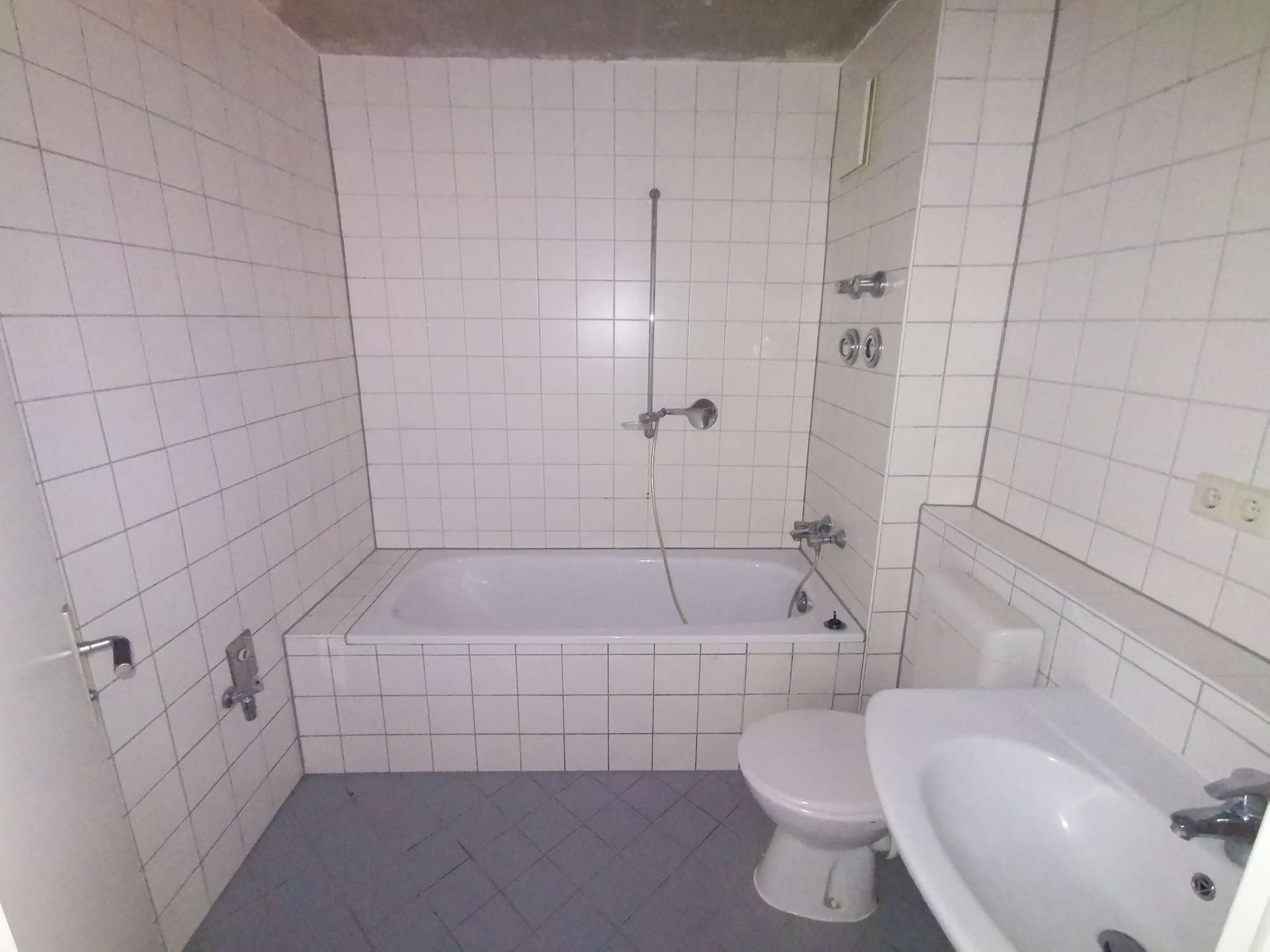 Bathroom with white tiled walls, bathtub, shower fixtures, and a toilet visible to the right.