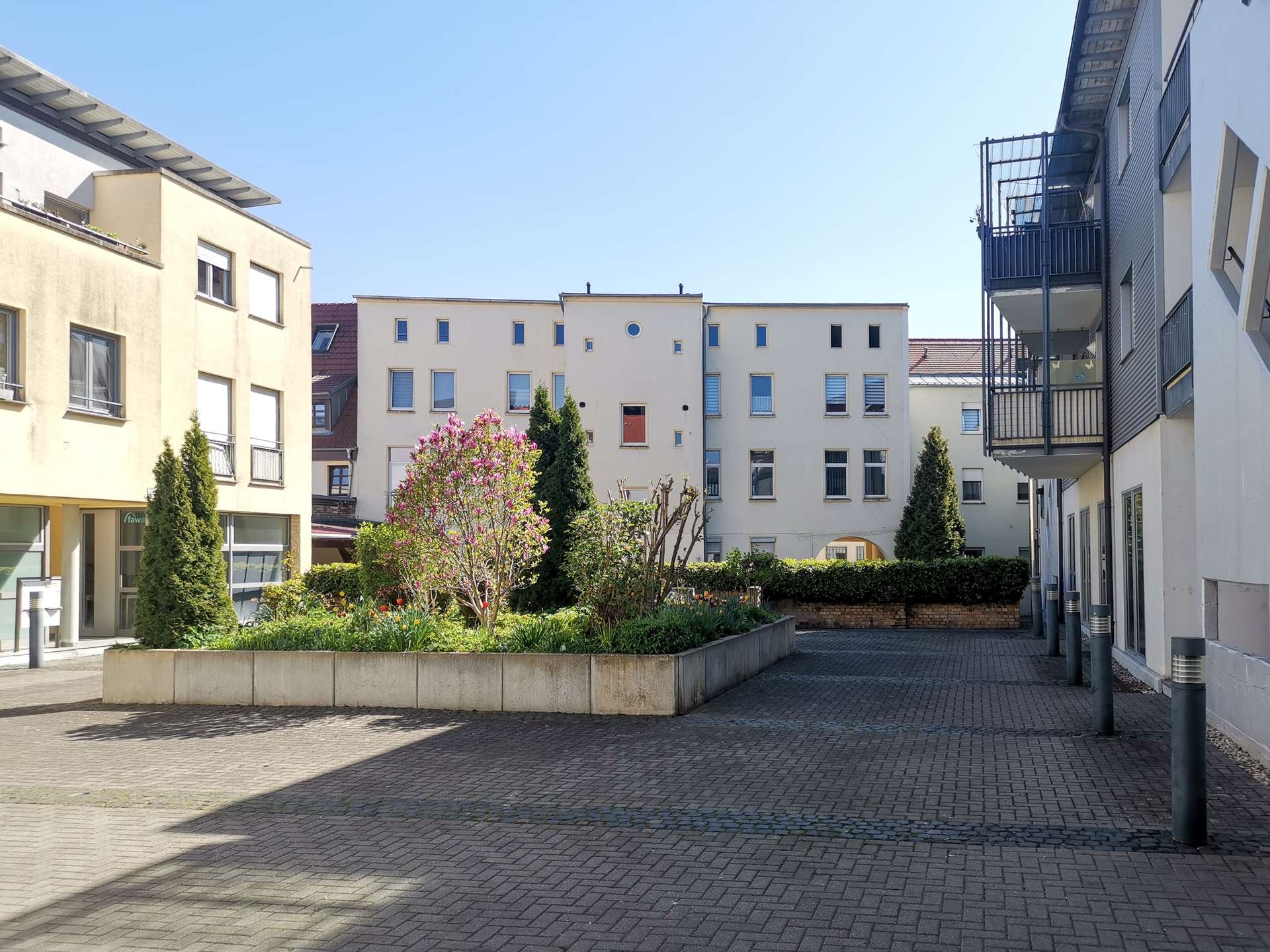 Court courtyard with beige apartment buildings, a central flower garden, and a blue sky above.