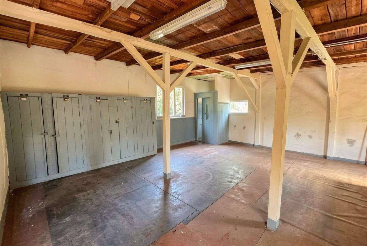 Room with gray lockers along the left wall and exposed wooden ceiling beams; industrial/warehouse feel.