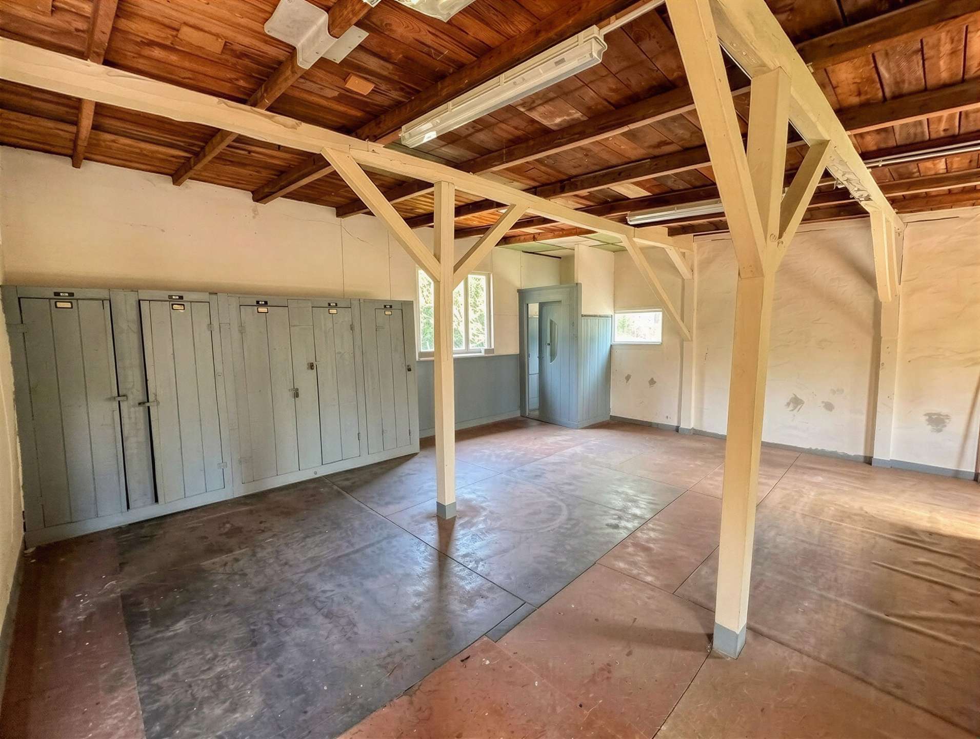 Room with gray lockers along the left wall and exposed wooden ceiling beams; industrial/warehouse feel.