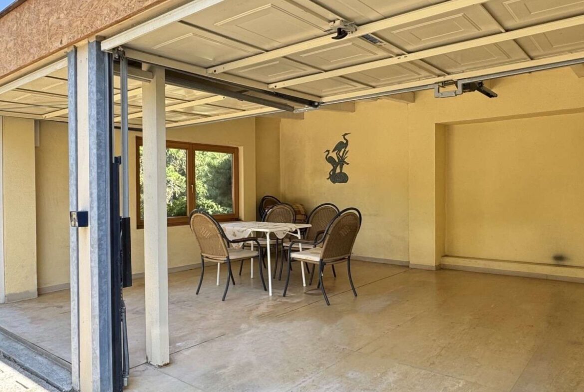 Covered garage dining area with a white table and wicker chairs, yellow walls and a bird mural.