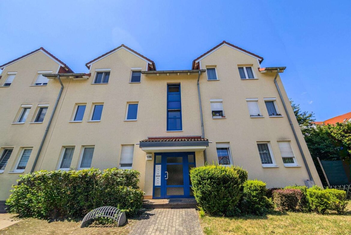 Beige three-story apartment building with a blue central entrance door, many white-framed windows, and a clear blue sky.