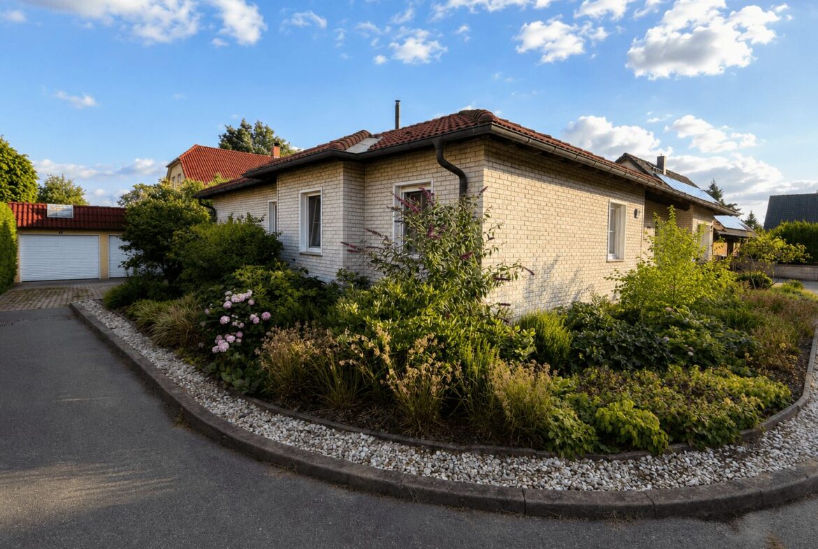 Single-story brick house with a red tile roof, surrounded by a lush garden and a curved driveway.