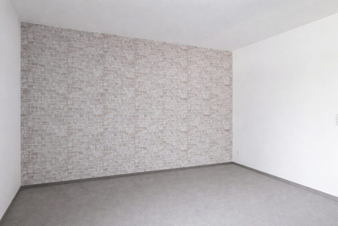 Empty room with white walls and a gray brick-pattern accent wall, and a gray floor.
