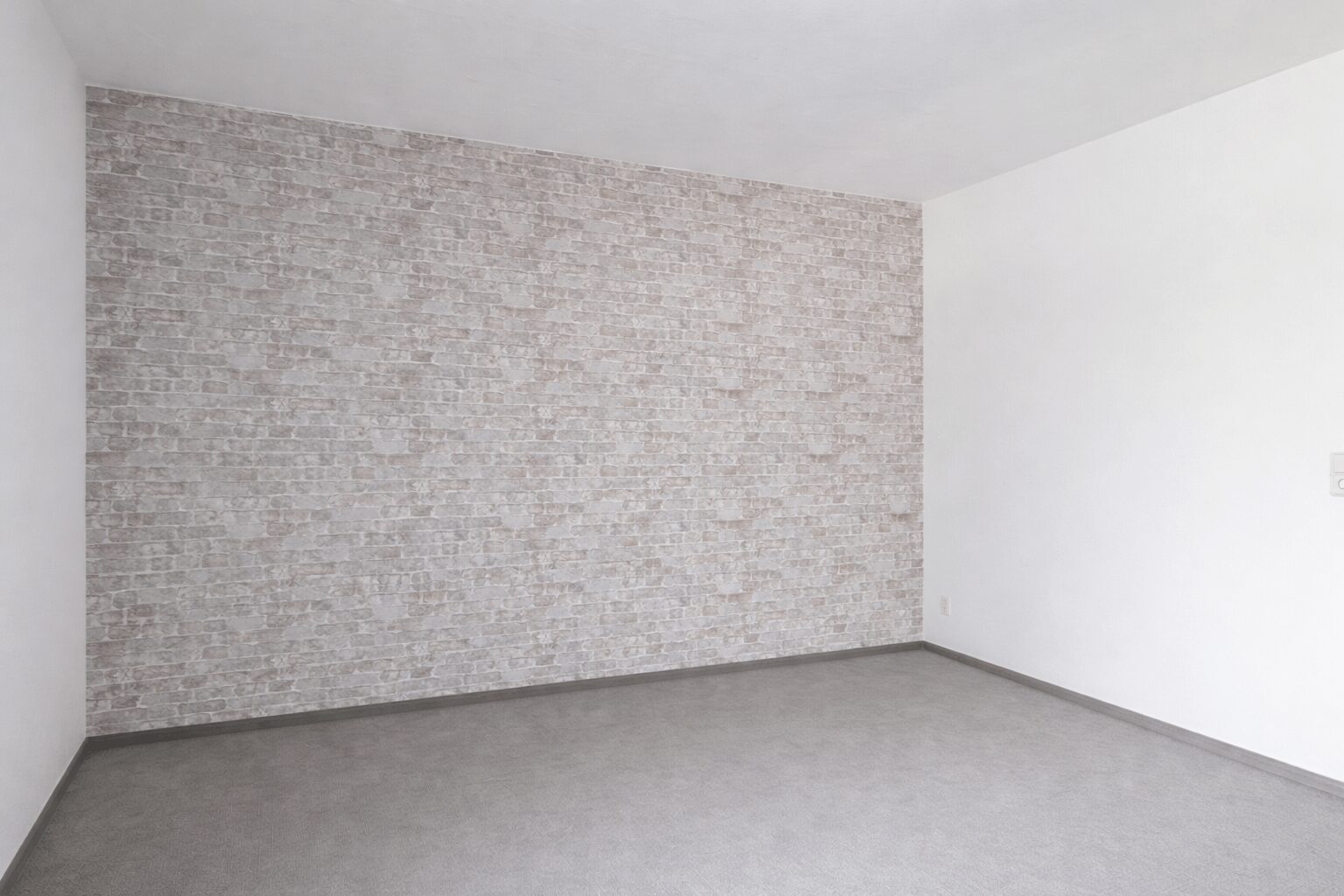 Empty room with white walls and a gray brick-pattern accent wall, and a gray floor.