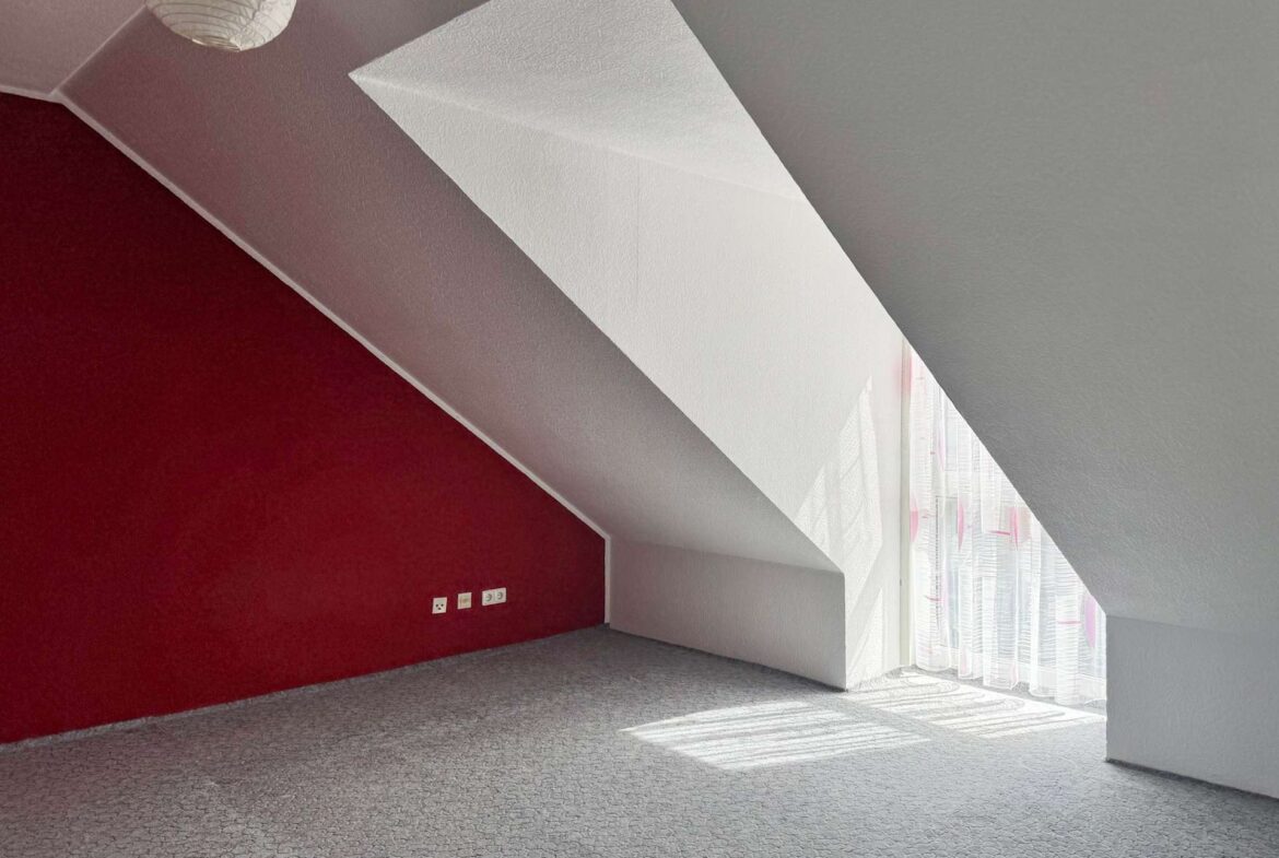 Interior room with a red accent wall on the left, a diagonal white architectural beam, and large windows with sheer curtains letting in daylight." (informative)