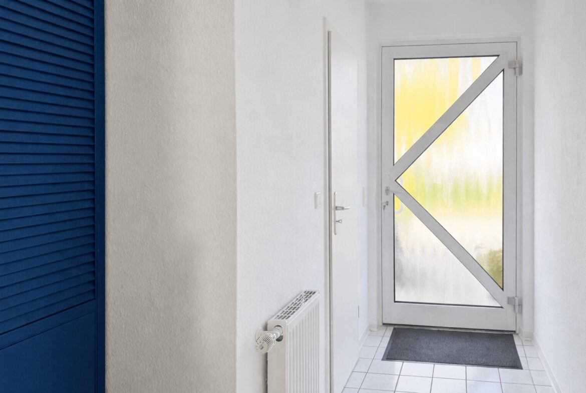 Narrow white hallway with a bold blue louvered closet on the left and a frosted glass entry door with a white X crossbar at the end.