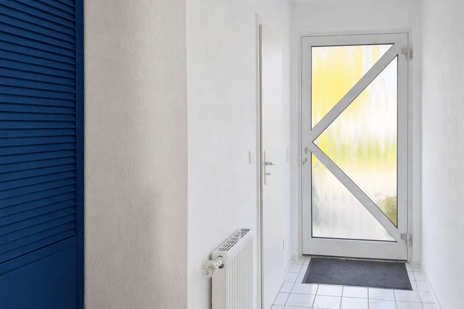 Narrow white hallway with a bold blue louvered closet on the left and a frosted glass entry door with a white X crossbar at the end.