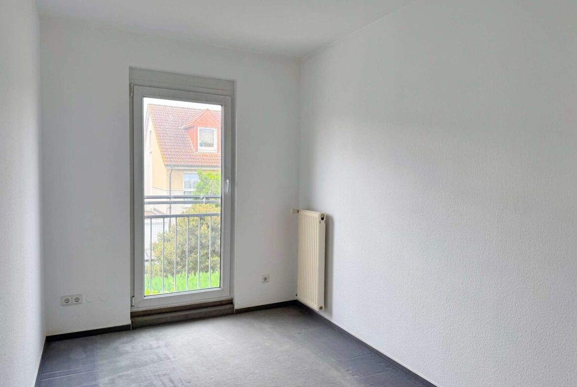 Empty, narrow room with a windowed door at the end and a radiator on the right wall.