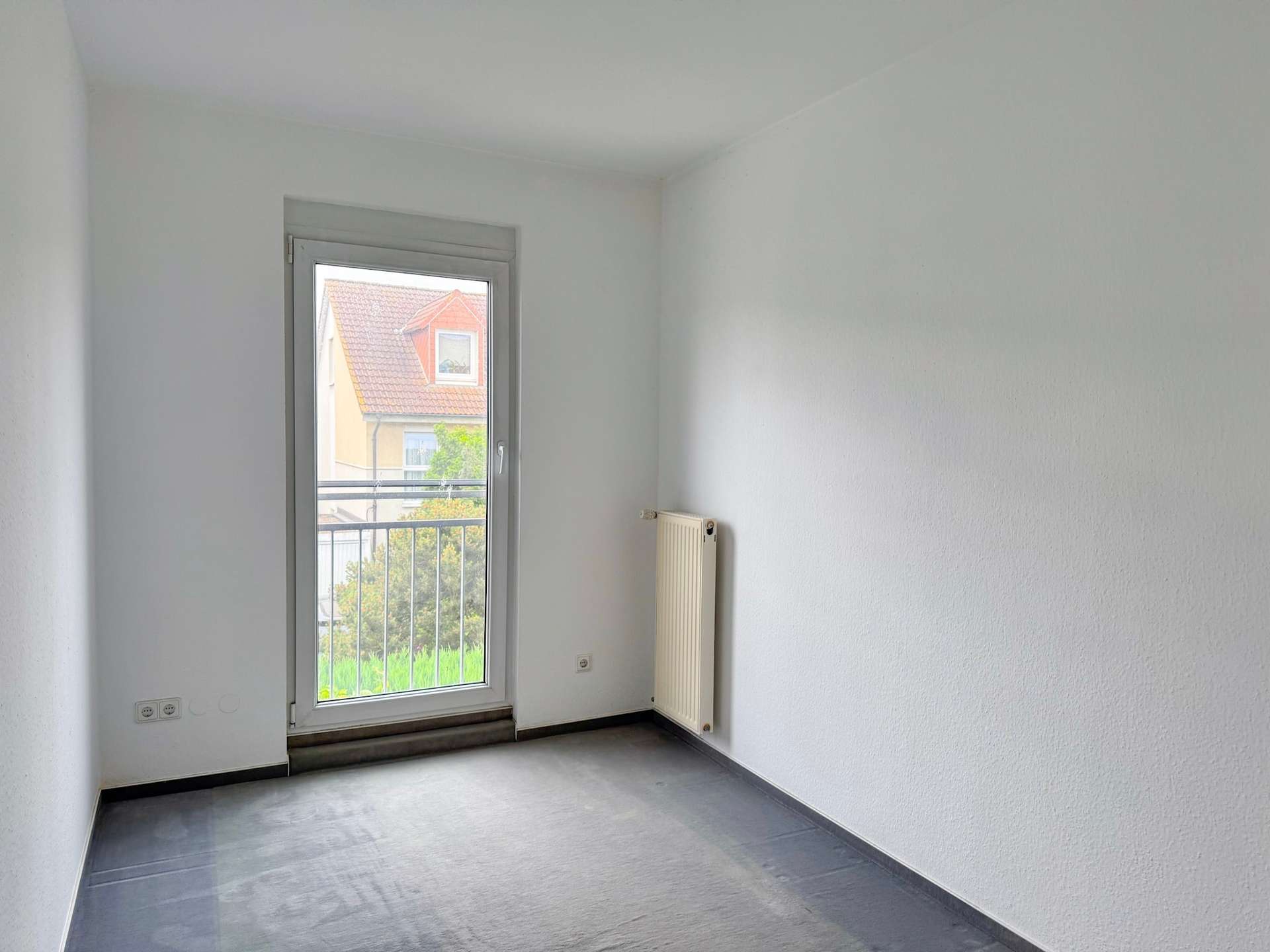 Empty, narrow room with a windowed door at the end and a radiator on the right wall.
