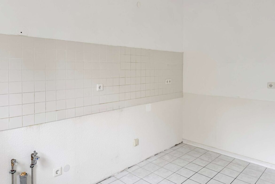 Empty kitchen/utility space with white tiled backsplash, tiled floor, and exposed plumbing on the left wall.