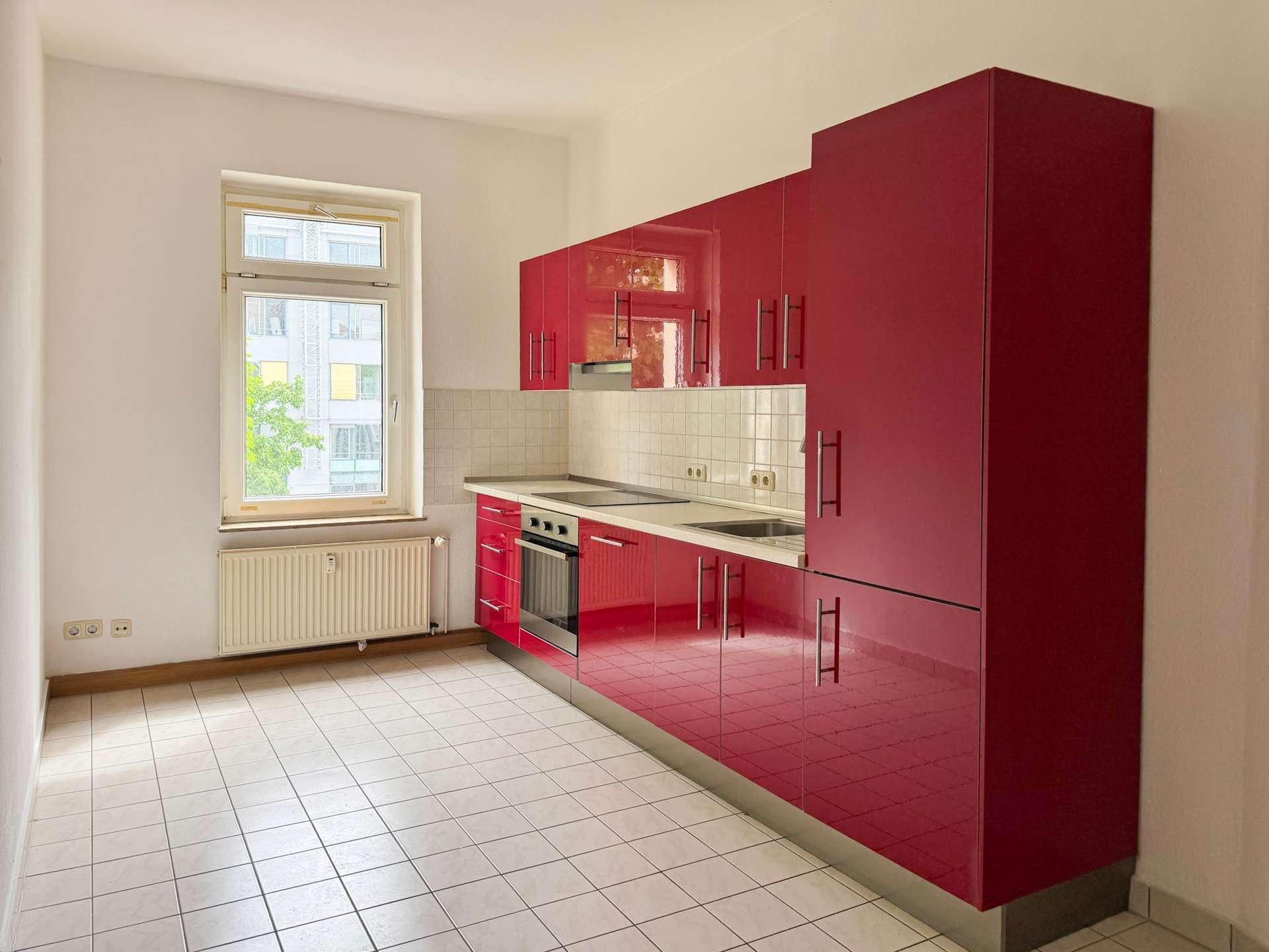 Modern kitchen with glossy red cabinets along the right wall, white tiled backsplash, and a stainless steel oven/stovetop.
