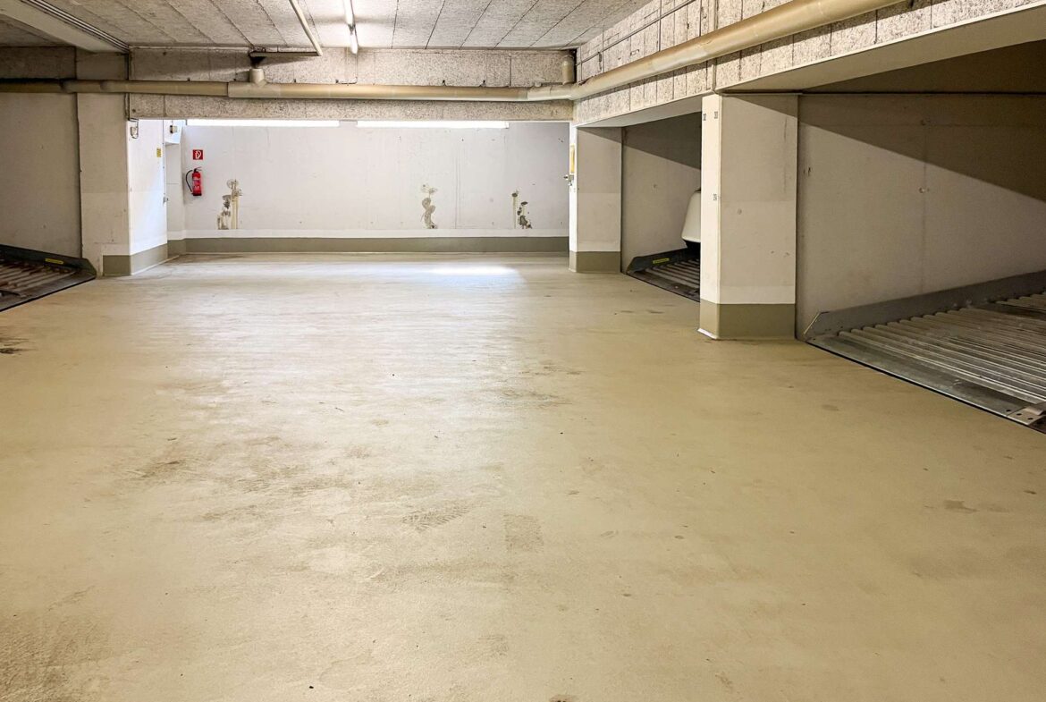 Underground parking garage with concrete walls and a ramp on the right; empty, well-lit space.