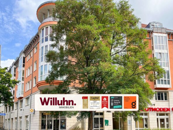 Orange multi-story building with large glass windows partially obscured by a green tree; storefront sign 'Willuhn Immobilien'.