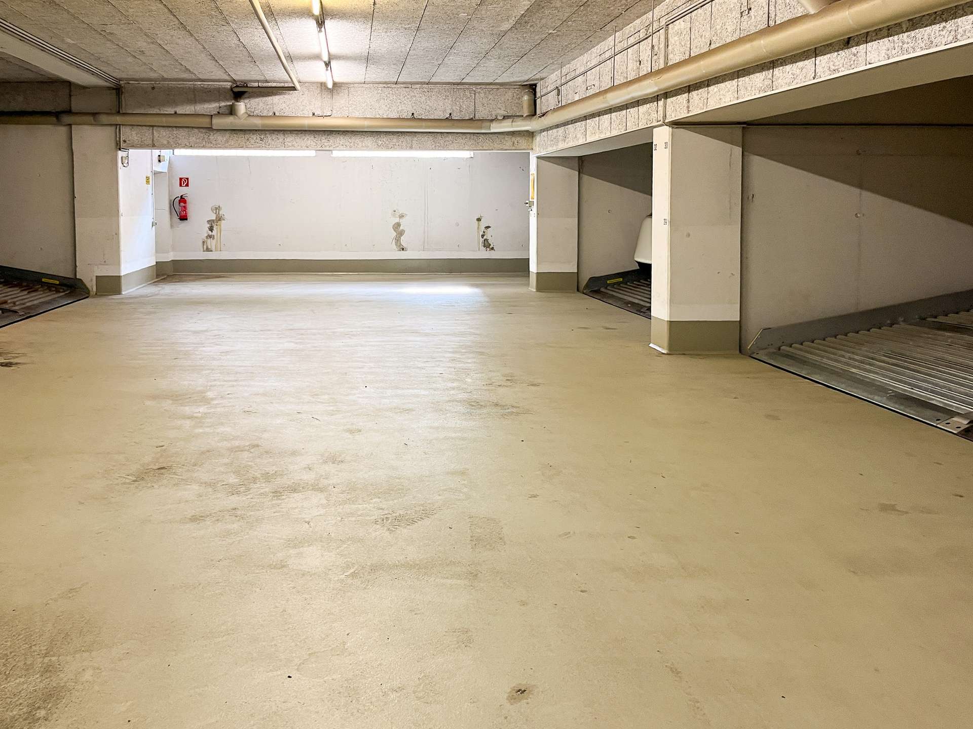 Underground parking garage with concrete walls, ramps, and fluorescent lighting; empty space in view.