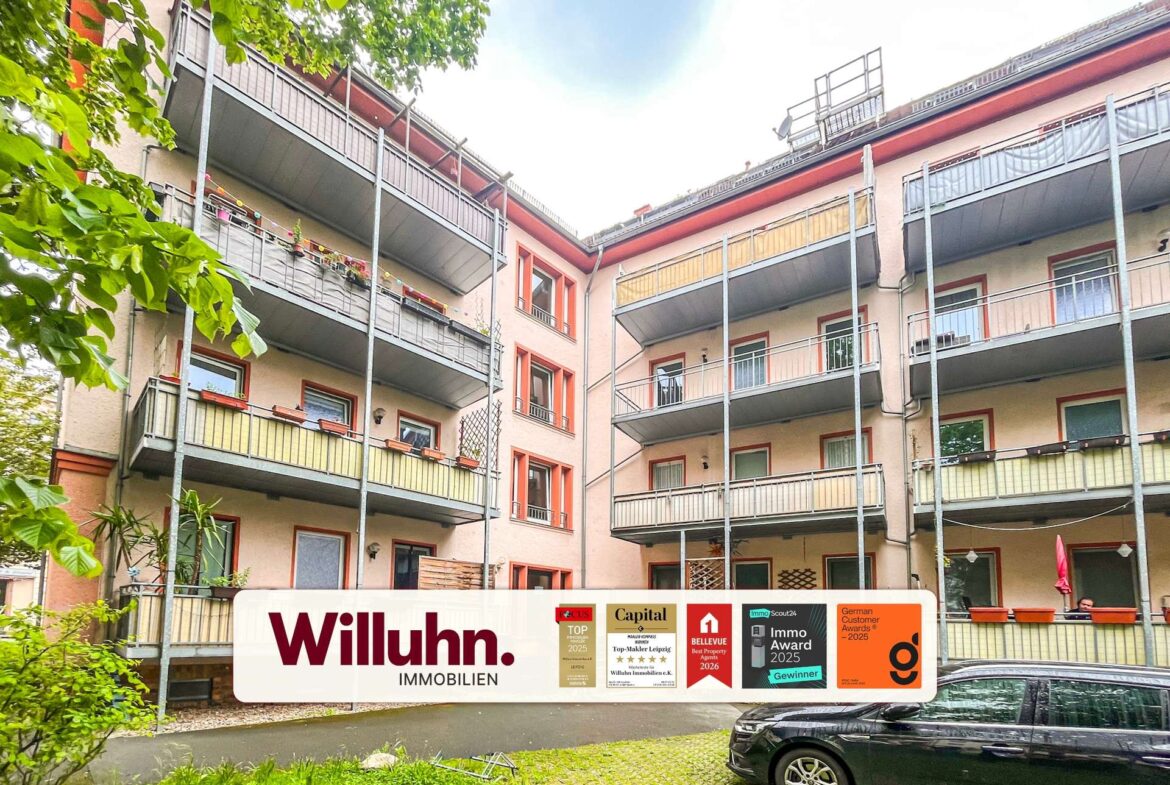 Residential apartment building with metal balconies and greenery, featuring a ground-level Willuhn Immobilien banner.