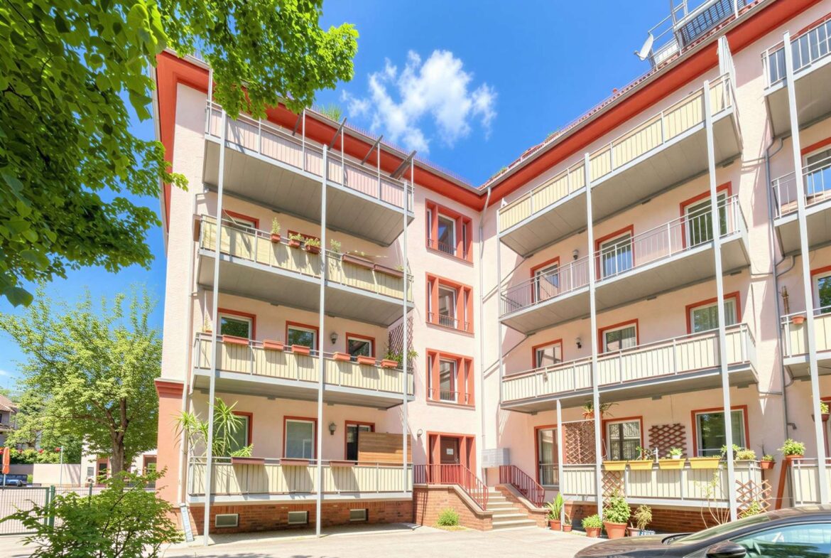 Apartment building with pink walls, red-trimmed balconies, and green plants under a bright blue sky