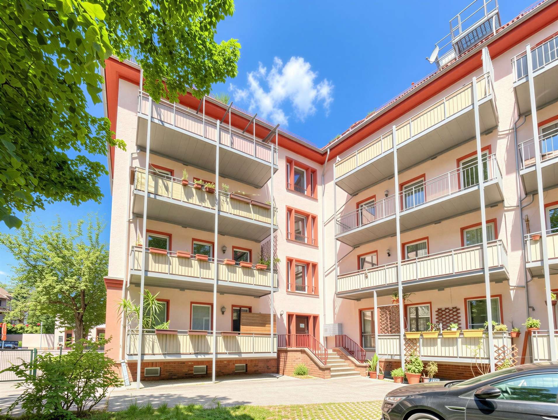 Apartment building with pink walls, red-trimmed balconies, and green plants under a bright blue sky