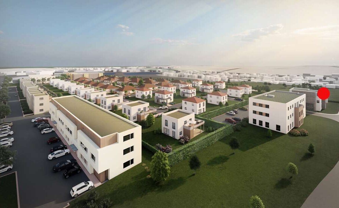 Aerial view of a modern housing development with white low-rise buildings, red-roofed homes, green lawns, and winding roads; a red marker highlights a building on the right.
