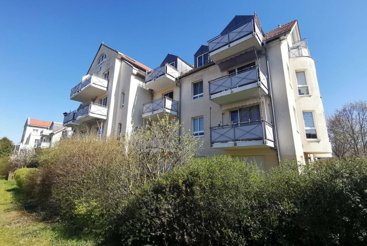 Apartment building with multiple balconies set against a clear blue sky, surrounded by shrubs and greenery in the foreground.