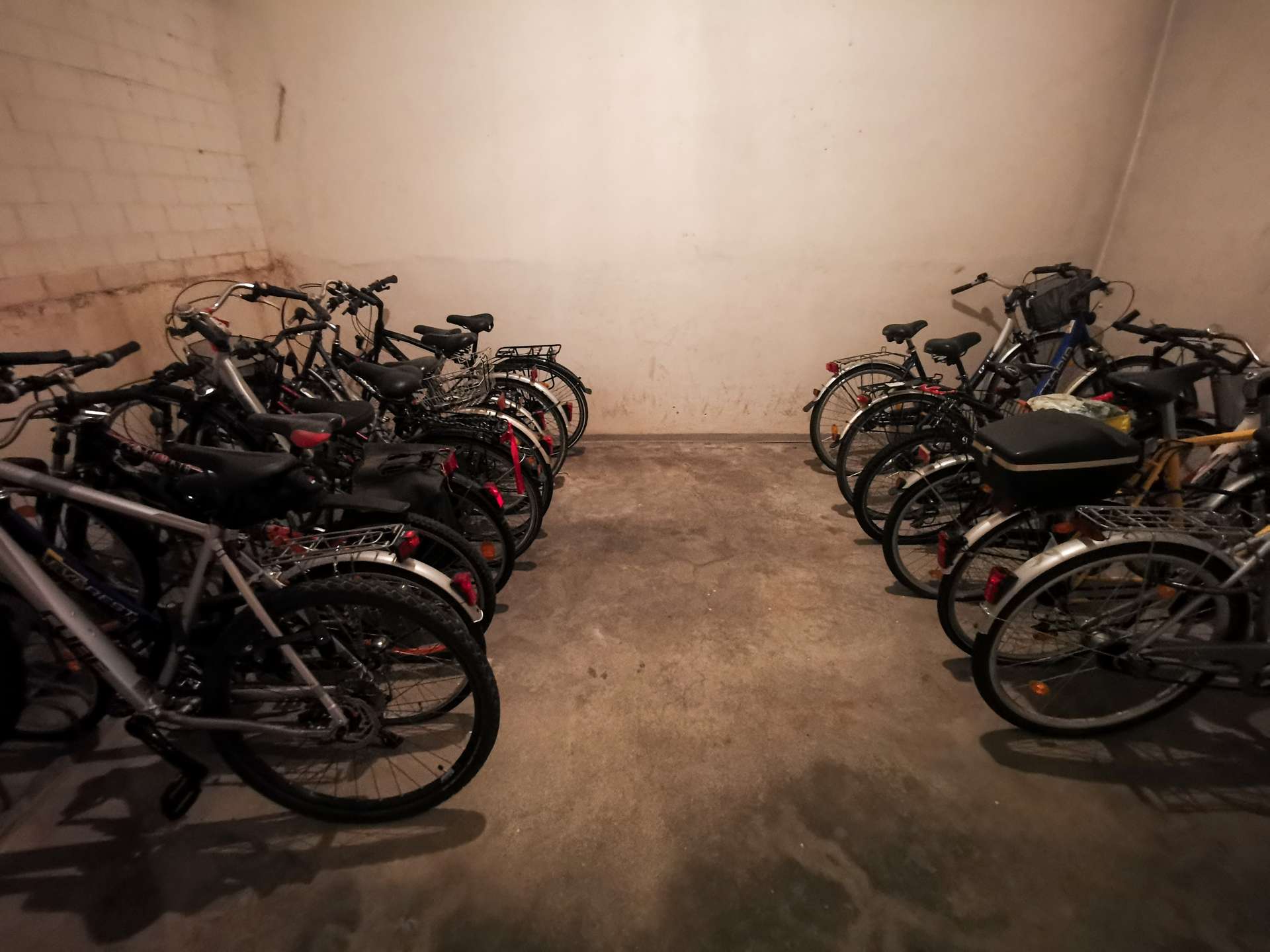 Bicycles parked in a dimly lit indoor parking area along brick walls on both sides