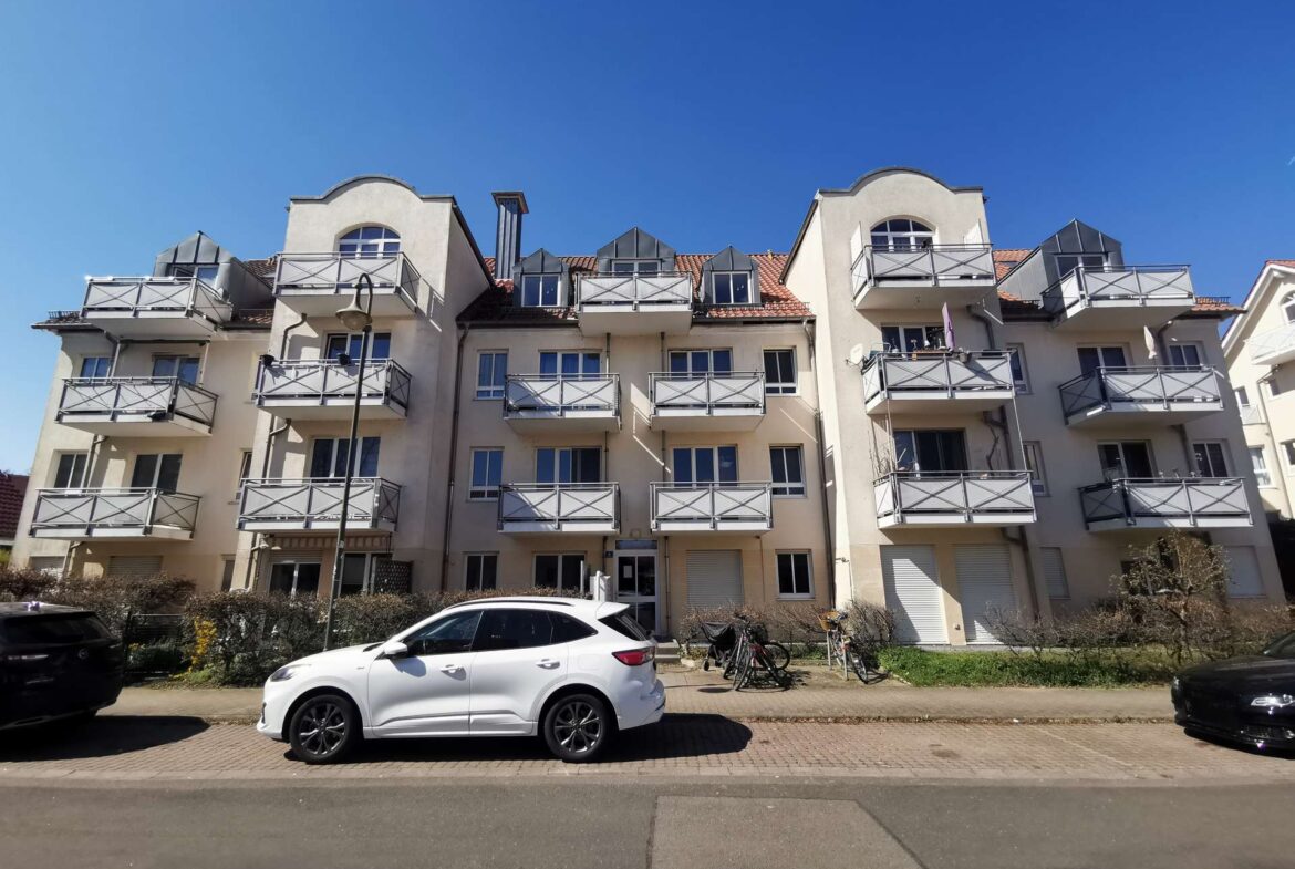 Beige apartment building with multiple balconies and curved roof elements under a clear blue sky.