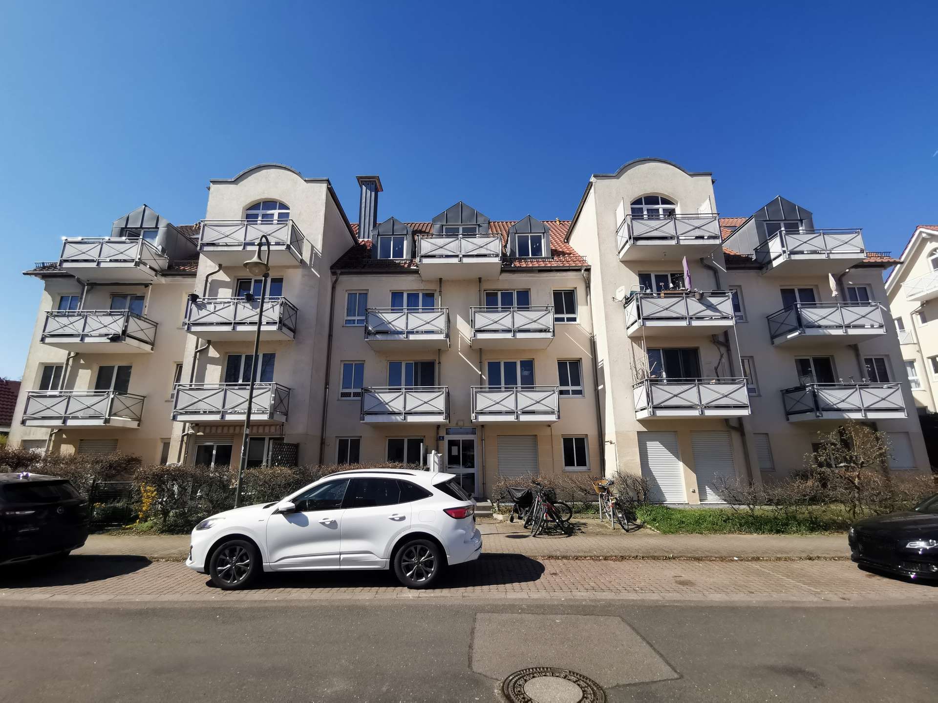Beige apartment building with multiple balconies and curved roof elements under a clear blue sky.
