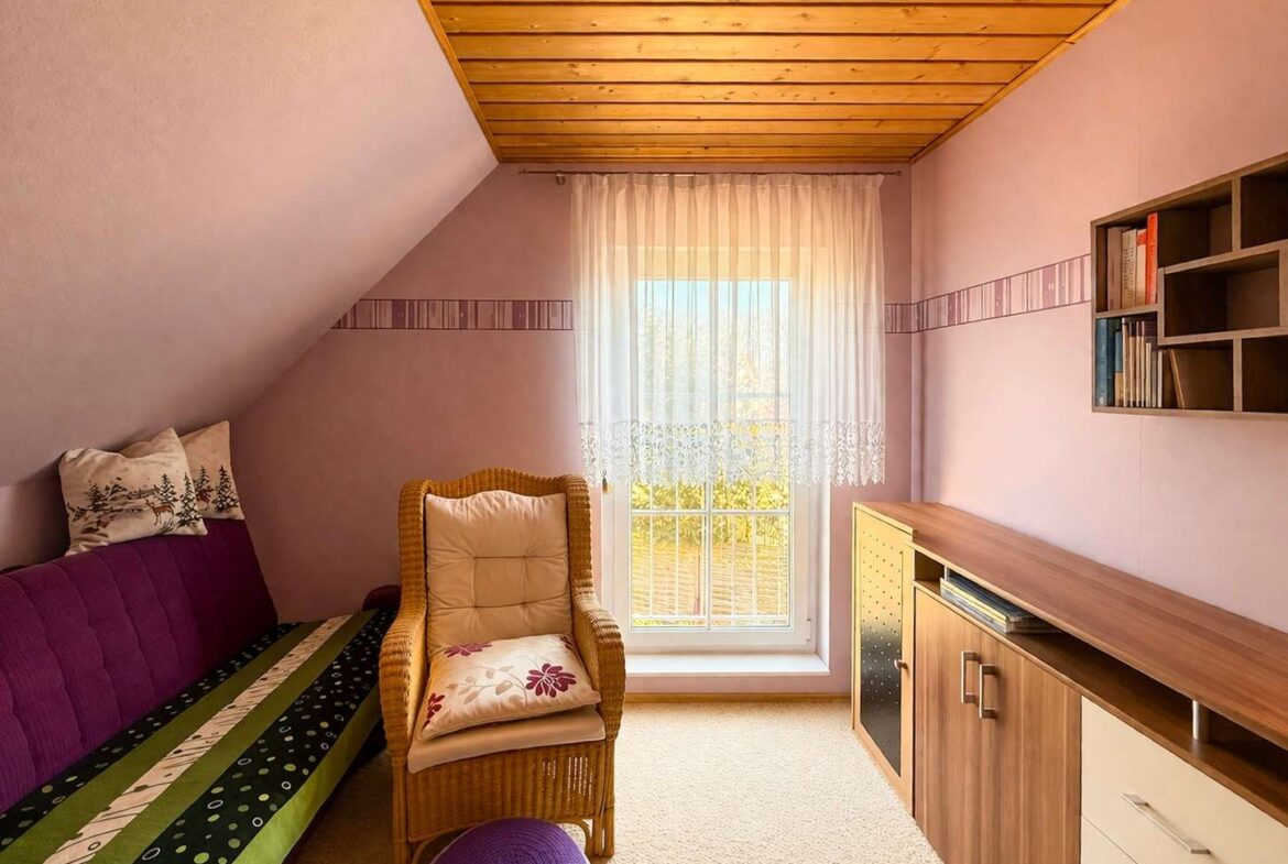 Cozy attic room with purple walls, a wooden beam ceiling, and a wicker chair by a sunlit window with lace curtains.