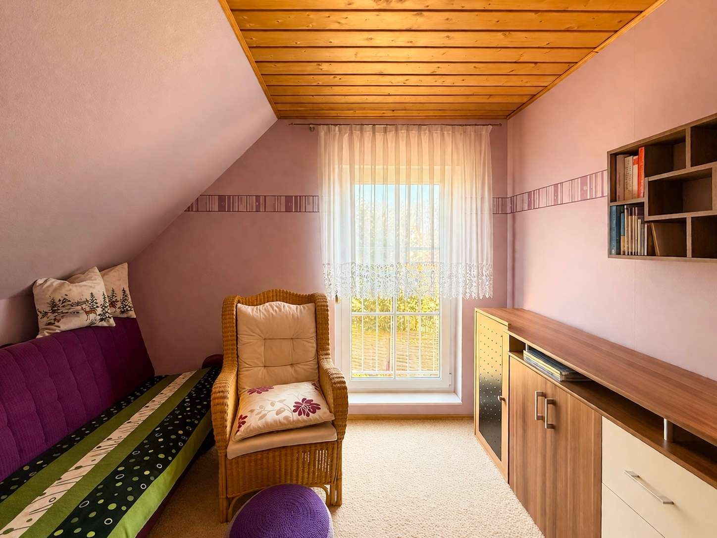 Cozy attic room with purple walls, a wooden beam ceiling, and a wicker chair by a sunlit window with lace curtains.