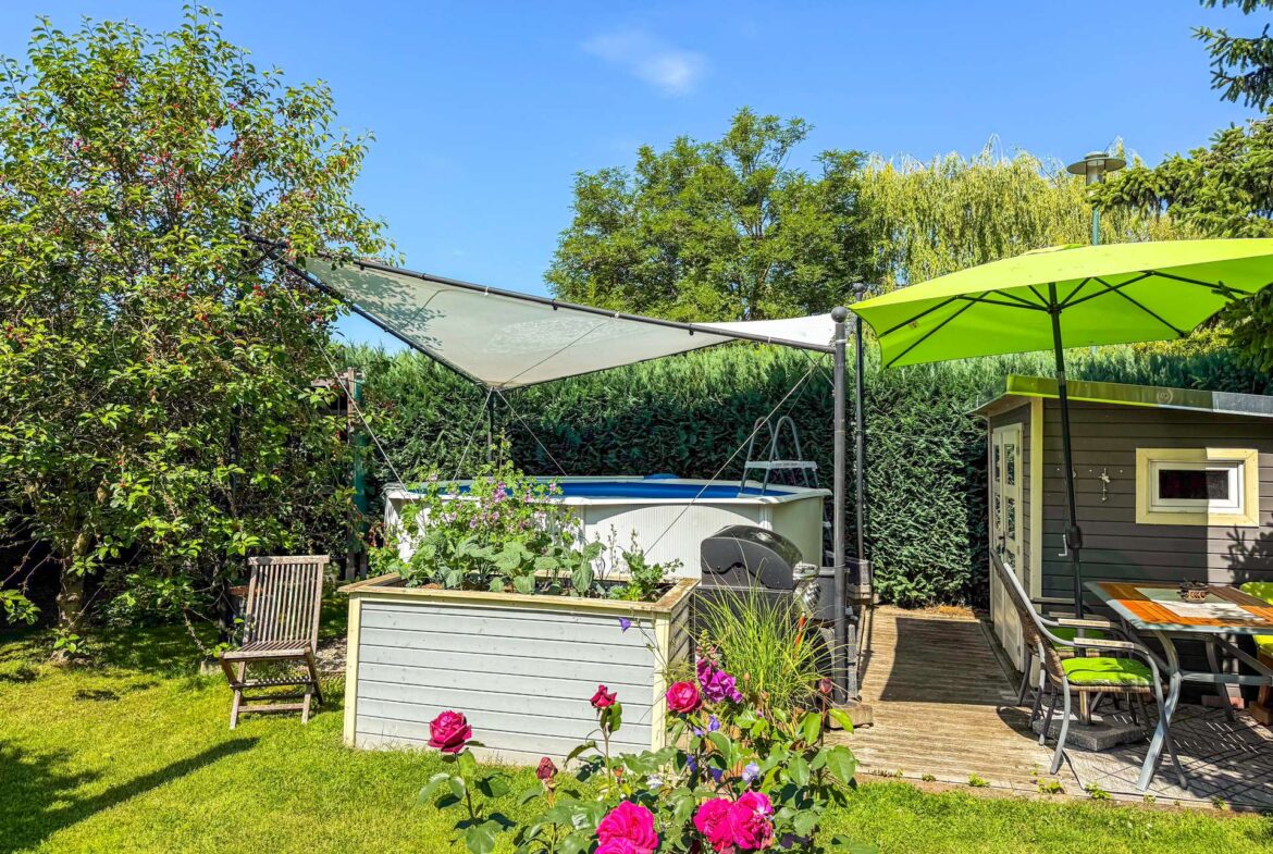 Sunny backyard scene with pink roses in the foreground, a raised planter box, wooden chairs, a pool, and a bright green patio umbrella on a deck under a blue sky.