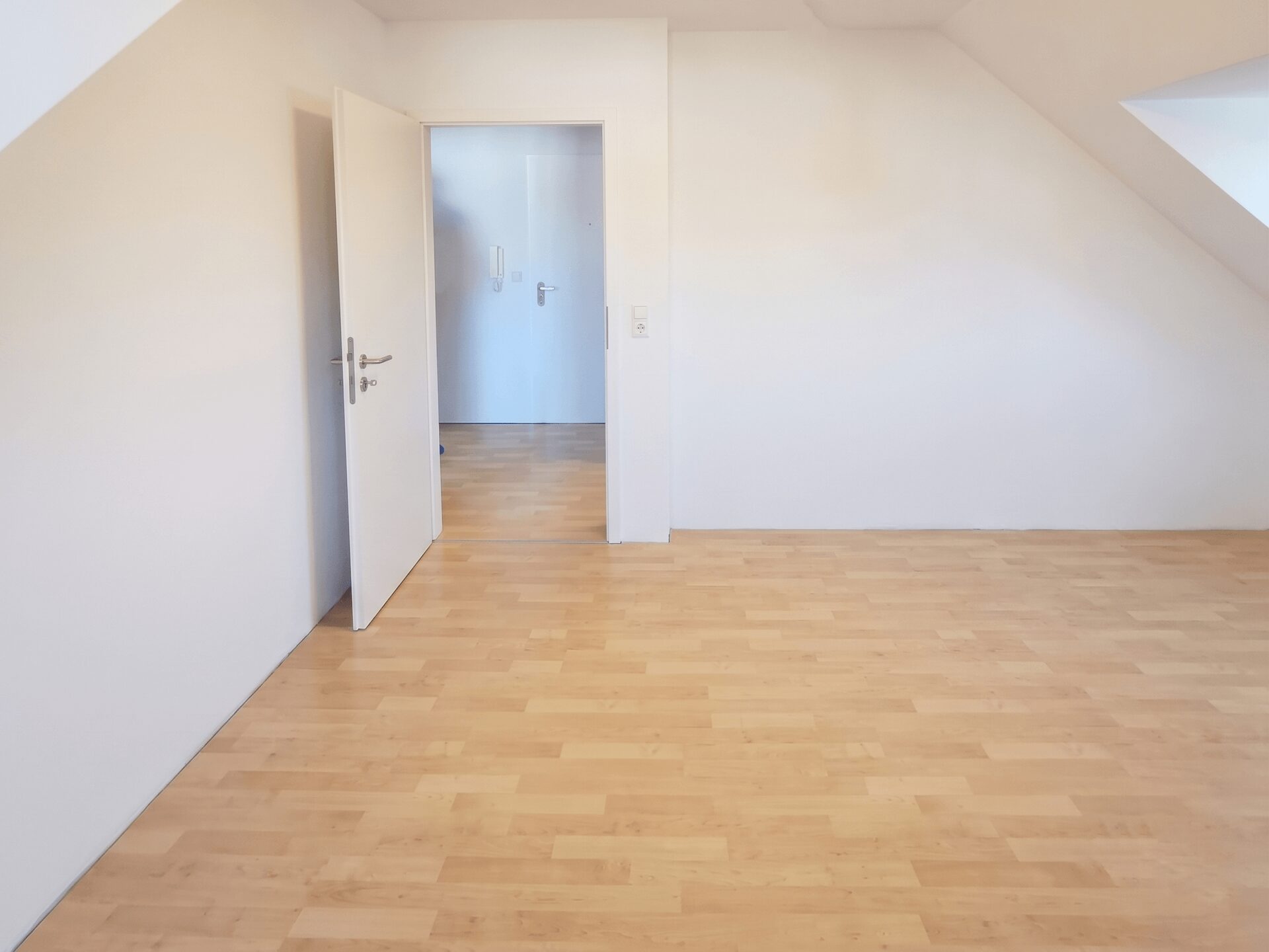 Empty white room with light wood floor and an open doorway to another small room or hallway.