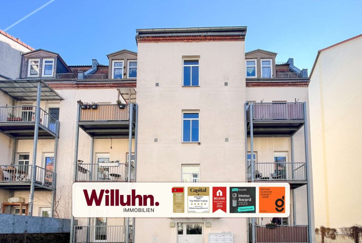 Apartment building with metal balconies and a large Willuhn Immobilien sign in front; blue sky above.