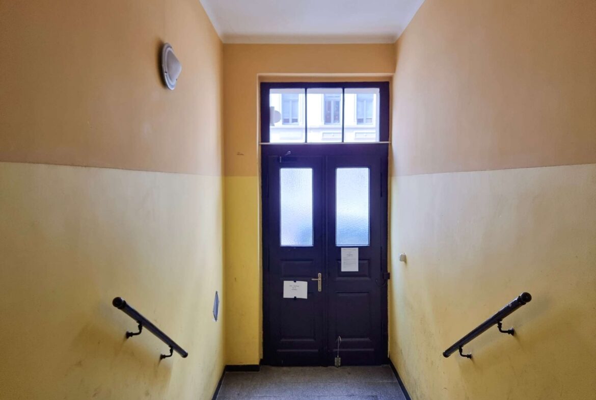 Narrow stairwell descending toward a dark door with frosted glass panels; yellow walls on both sides and metal handrails.
