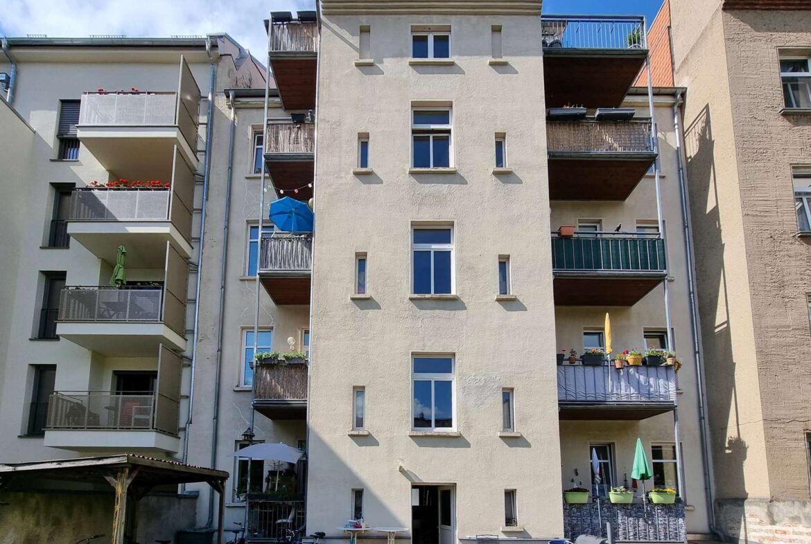 Beige apartment building with multiple balconies and potted plants along a central courtyard.IMPLIED: residential complex full of balconies and plants