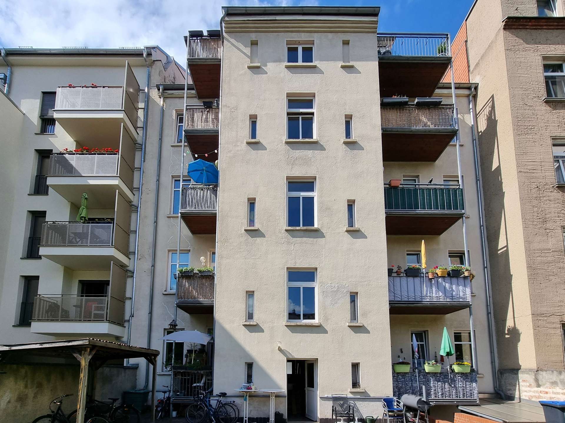 Beige apartment building with multiple balconies and potted plants along a central courtyard.IMPLIED: residential complex full of balconies and plants