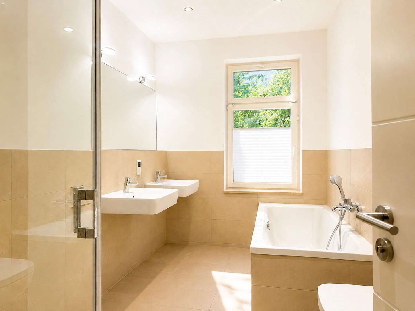 Bright modern bathroom with two wall-mounted sinks, large mirror, and glass shower enclosure on beige tile walls and floor.