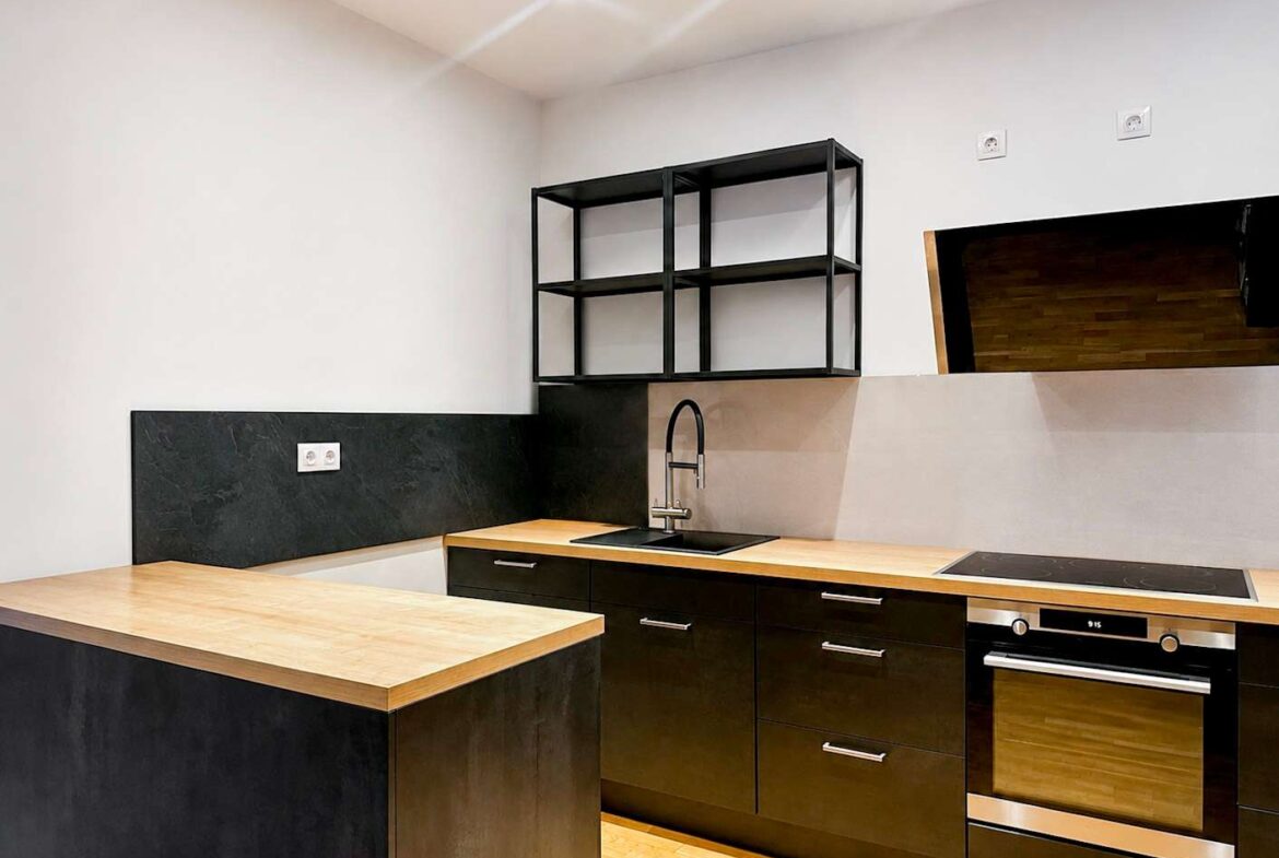 Modern kitchen with black lower cabinets, wooden countertops, and a built-in oven; black metal open shelves above the sink area.