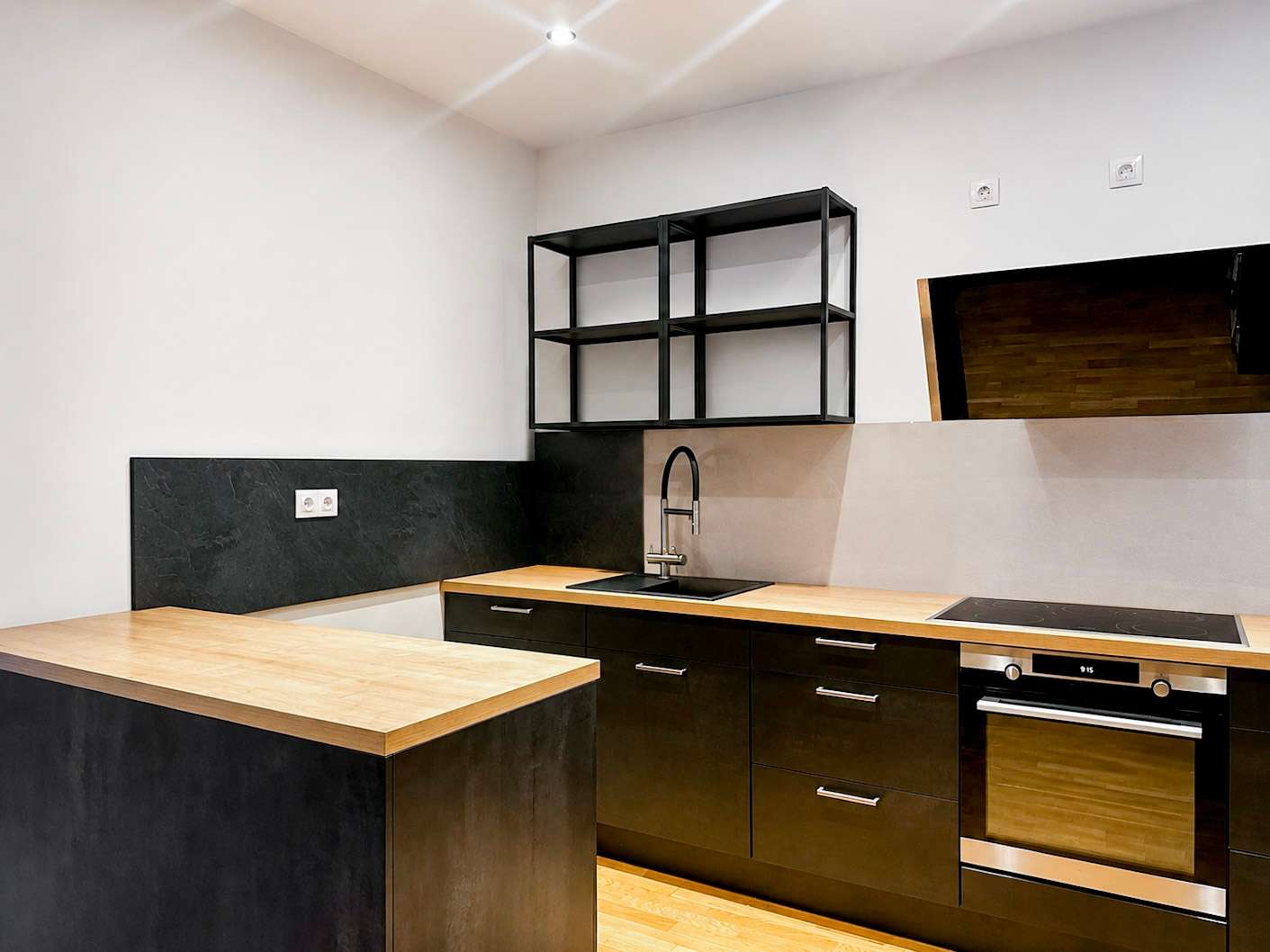 Modern kitchen with black lower cabinets, wooden countertops, and a built-in oven; black metal open shelves above the sink area.