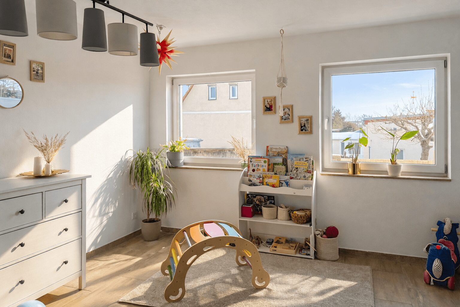 Bright playroom with a white dresser, two windows, plants, and a wooden curved toy on a beige rug.
