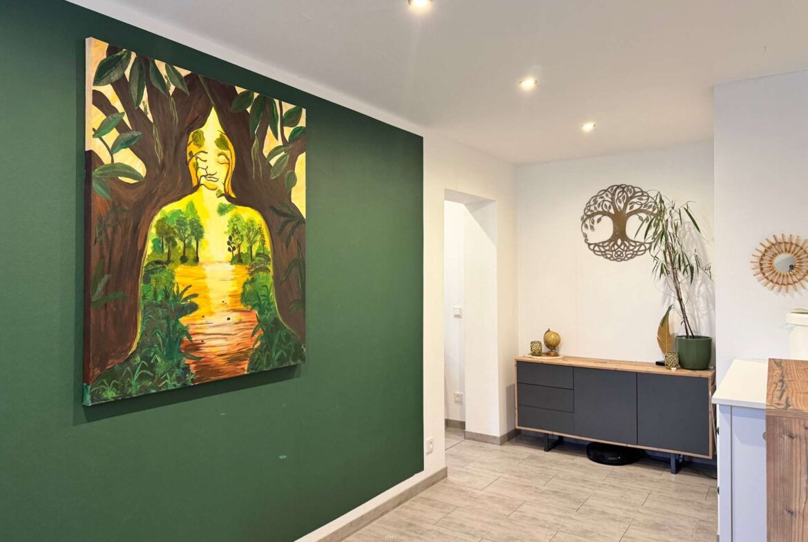 Large colorful painting of a seated Buddha figure among trees on a dark green accent wall in a modern hallway, with a console and plants nearby.