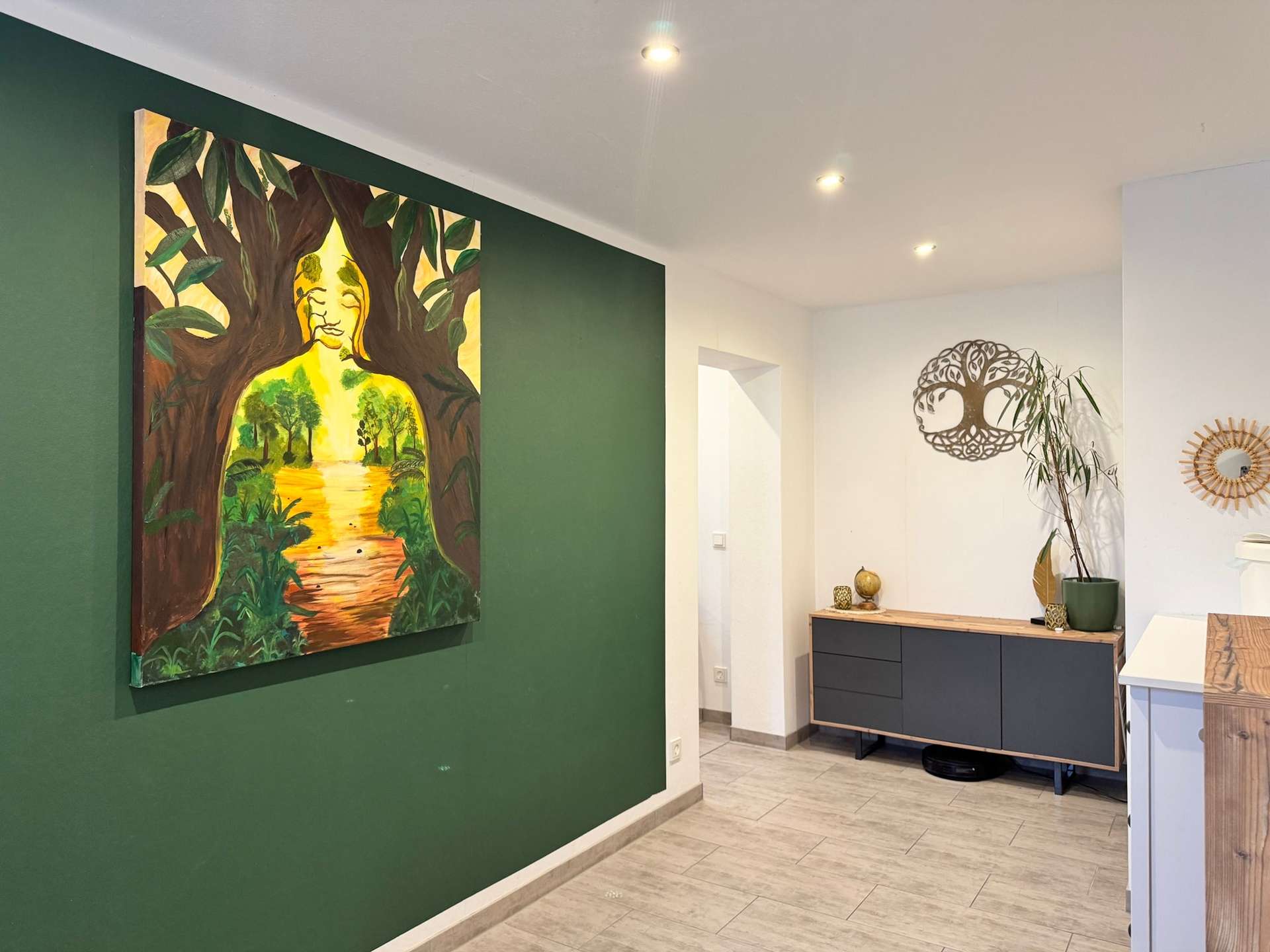 Large colorful painting of a seated Buddha figure among trees on a dark green accent wall in a modern hallway, with a console and plants nearby.