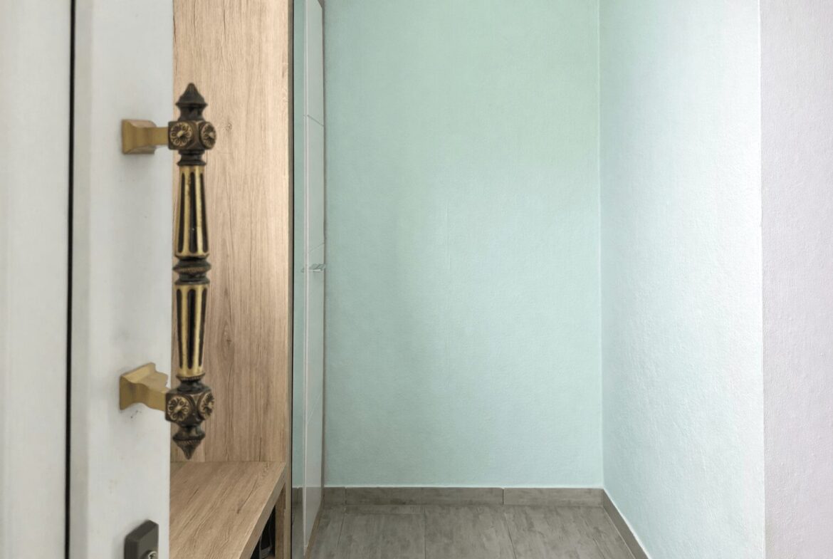 Ornate brass door handle on a white door beside a wooden bench in a pale mint hallway.