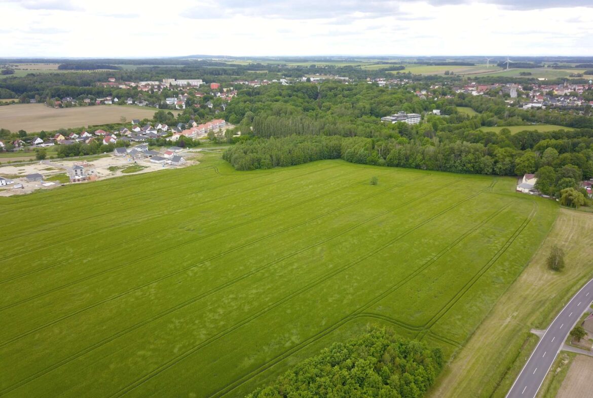 Aerial view of farmland with green fields, a small town edge, and a highway on the right.