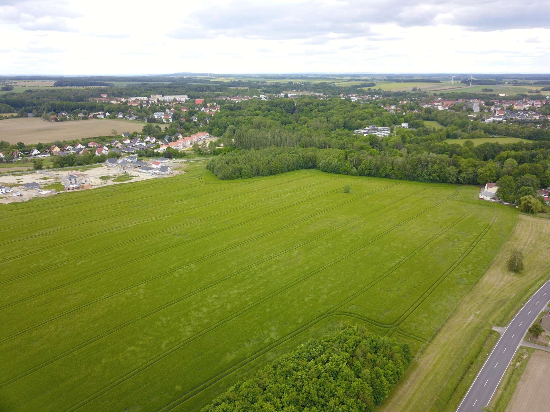 Aerial view of farmland with green fields, a small town edge, and a highway on the right.