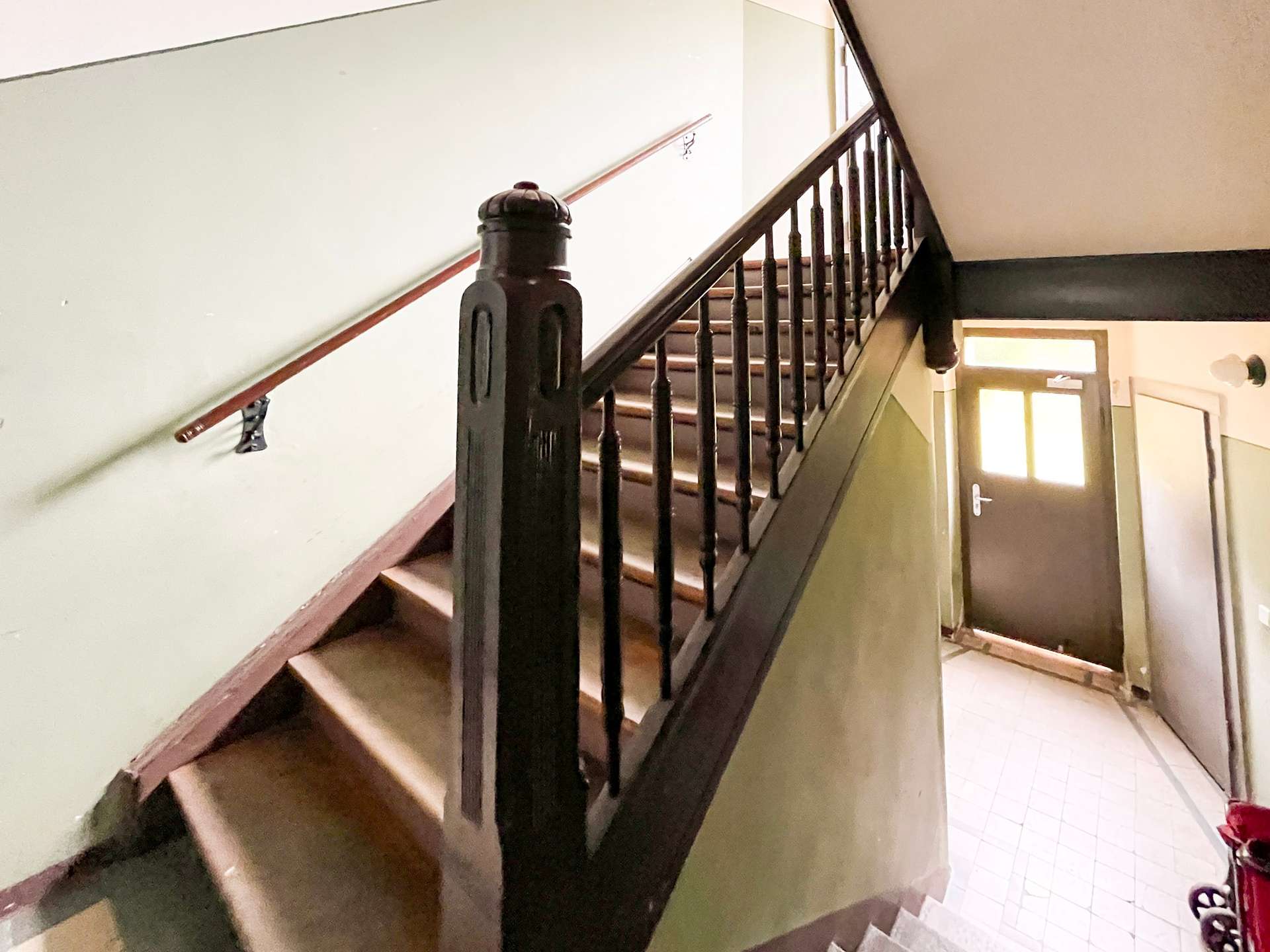 Indoor staircase with a dark wooden banister and spindles, green walls, and a door visible at the bottom right.